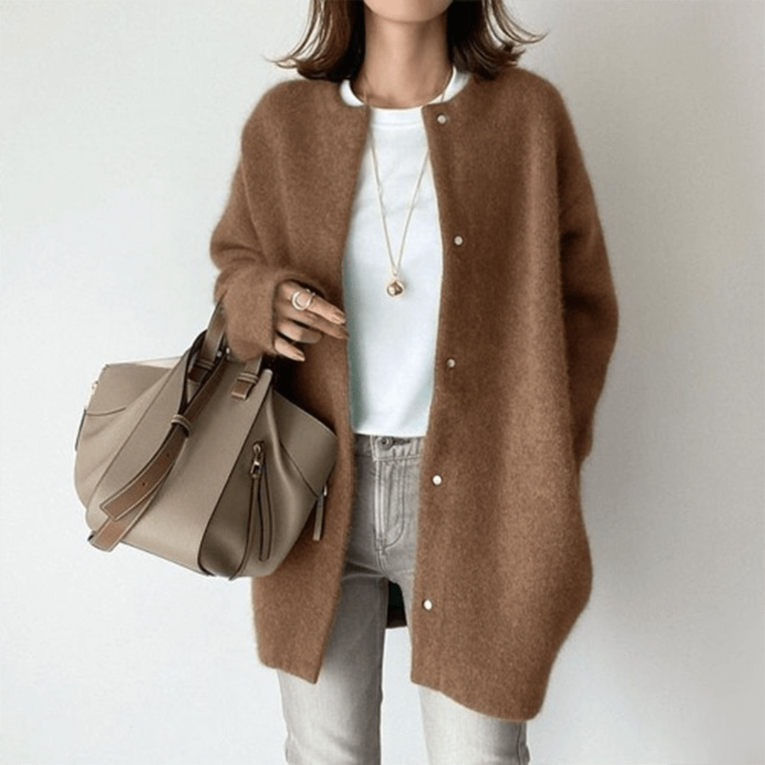 Person wearing a brown cardigan holding a beige handbag on a plain background