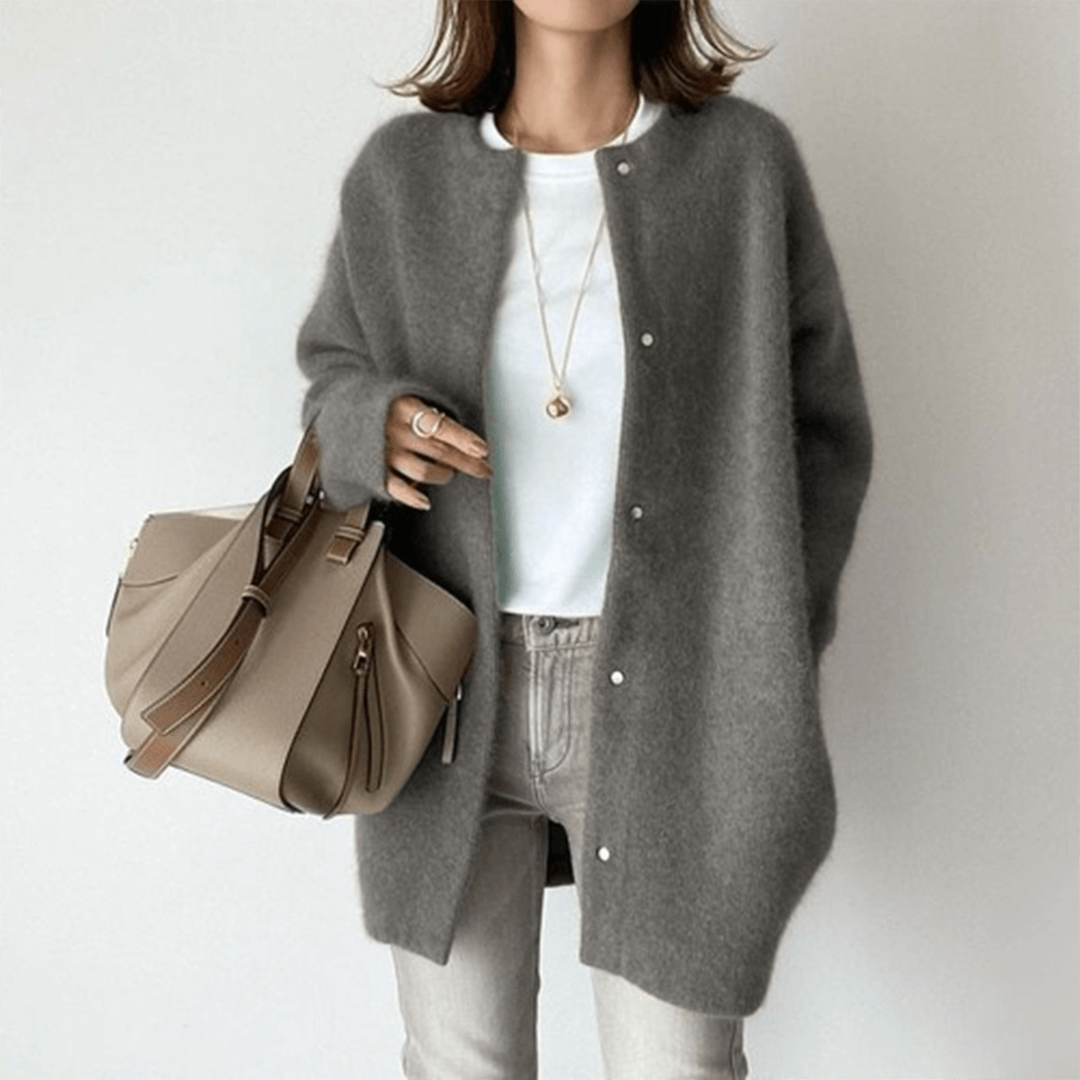 Person wearing a gray cardigan holding a beige handbag on a plain background