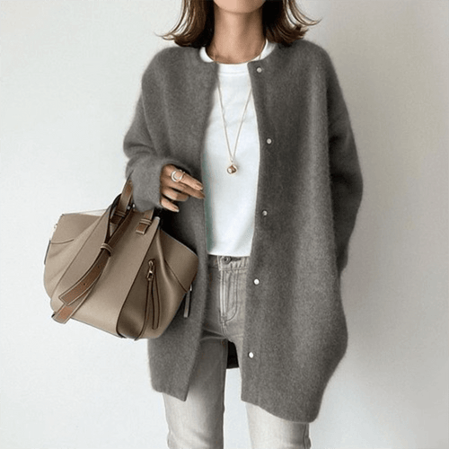 Person wearing a gray cardigan holding a beige handbag on a plain background